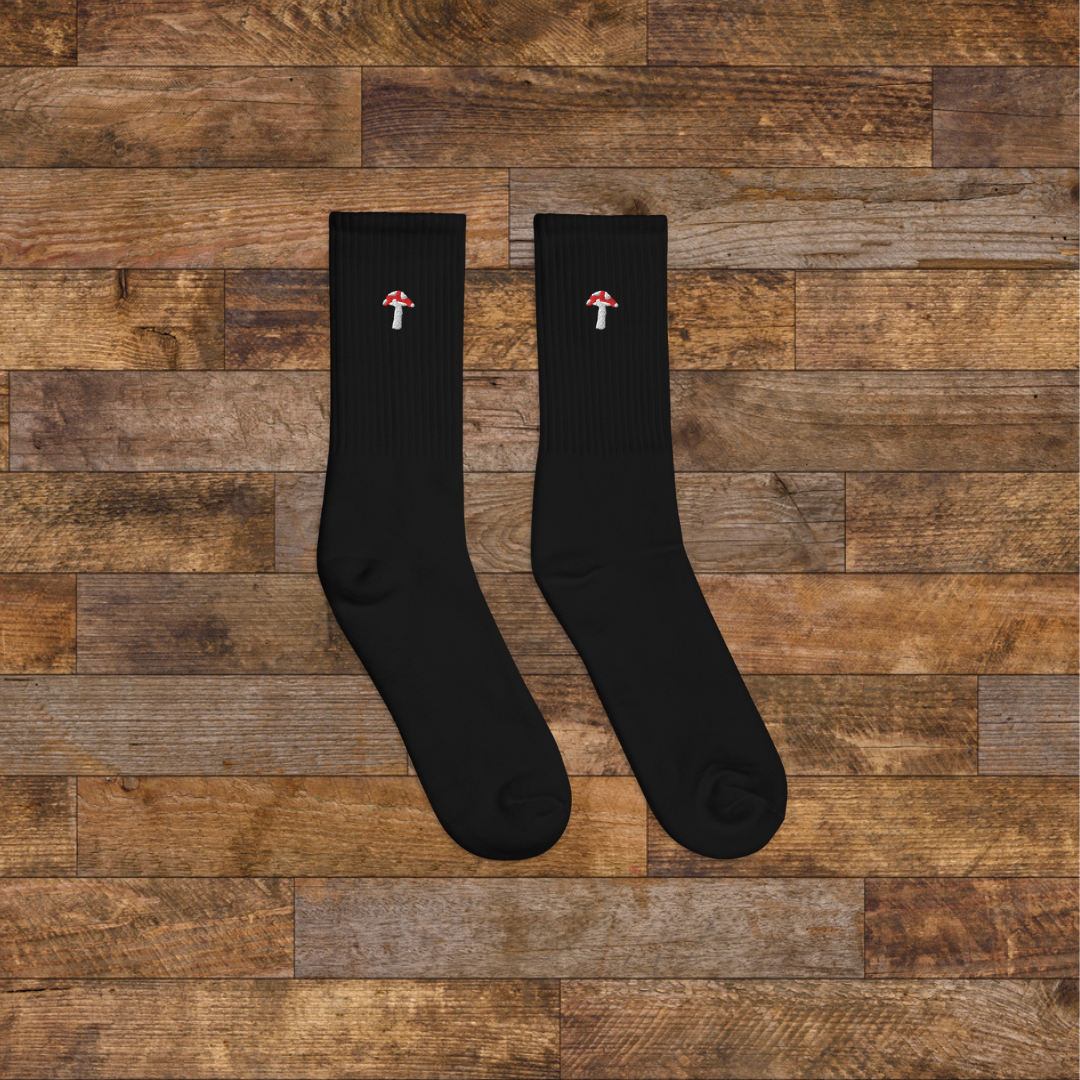 right black Embroidered Mushroom Crew Socks - ribbed knit with fly agaric red mushroom ankle design, wooden background.