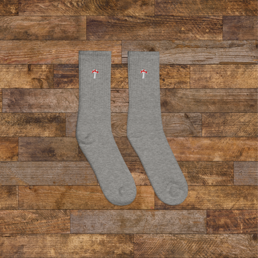 right grey Embroidered Mushroom Crew Socks - ribbed knit with fly agaric red mushroom ankle design, wooden background.