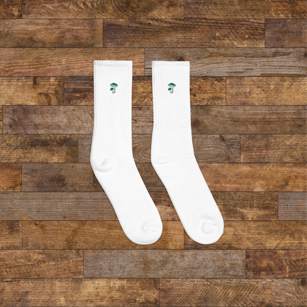 Right White Embroidered Mushroom Crew Socks - ribbed knit with Russula green mushroom ankle design, wooden background.