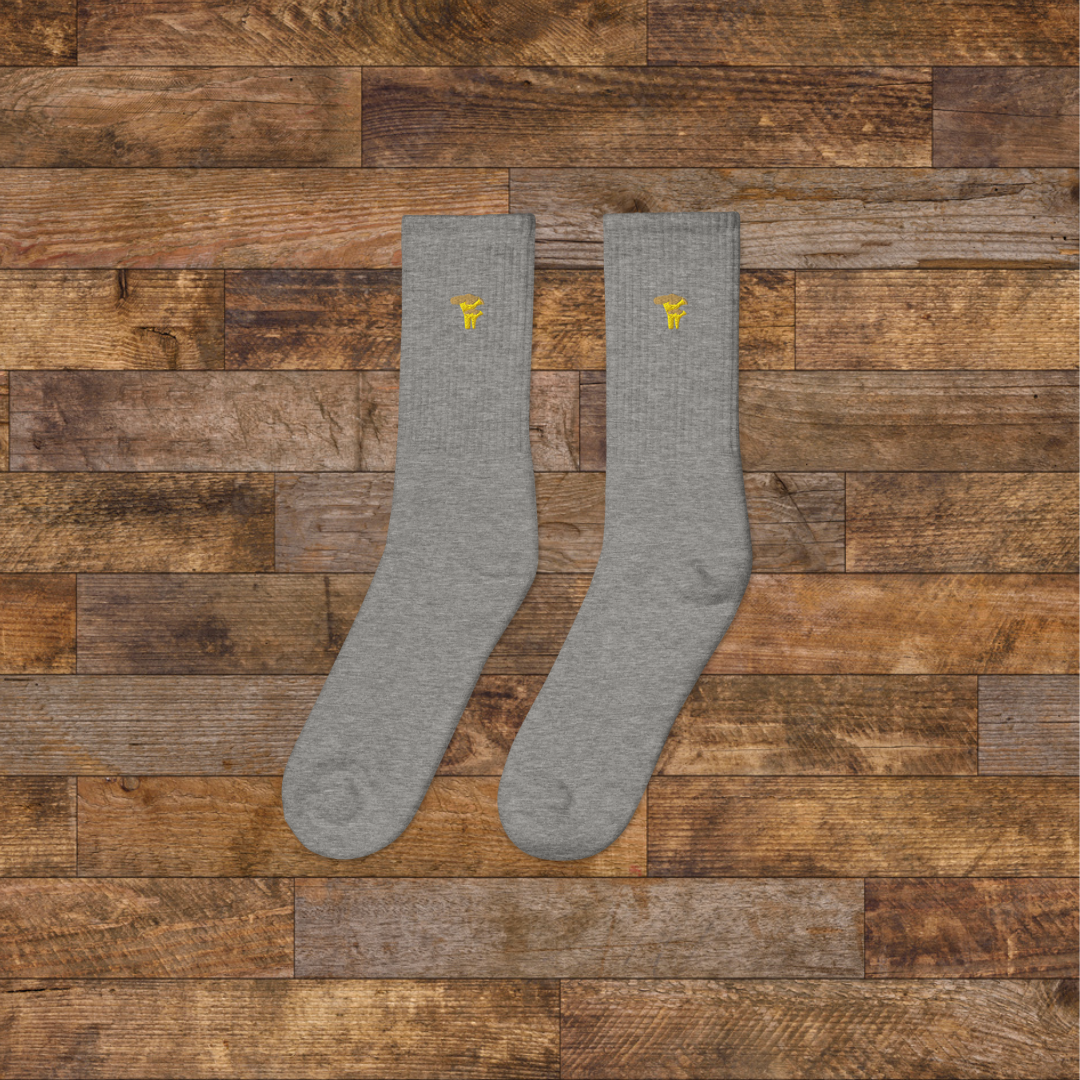 Left grey Embroidered Mushroom Crew Socks - ribbed knit with Chanterelle yellow mushroom ankle design, wooden background.