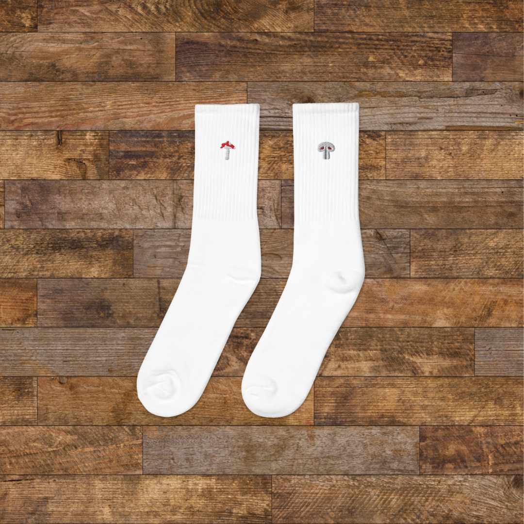left white Embroidered Mushroom Crew Socks - ribbed knit with fly agaric red and paris grey mushroom ankle design, wooden background.