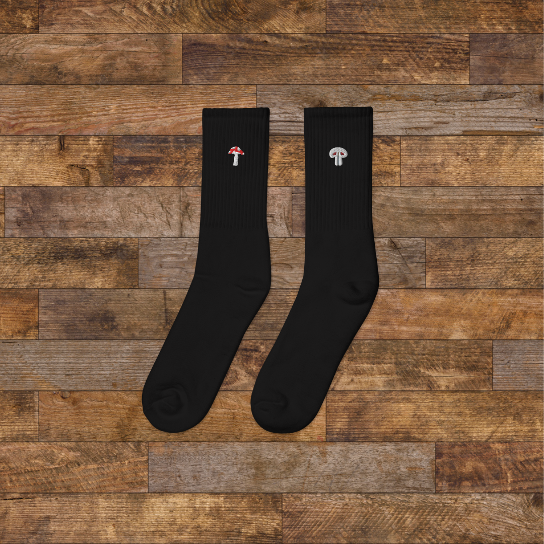 left black Embroidered Mushroom Crew Socks - ribbed knit with fly agaric red and paris grey mushroom ankle design, wooden background.