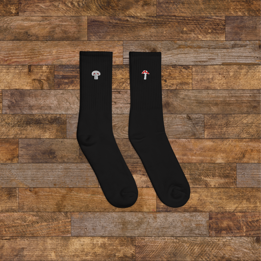 right black Embroidered Mushroom Crew Socks - ribbed knit with fly agaric red and paris grey mushroom ankle design, wooden background.