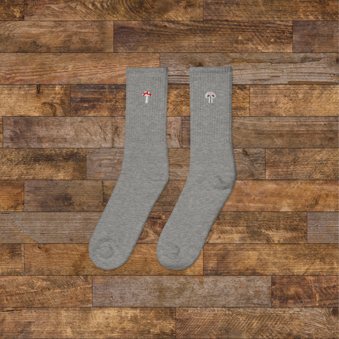 left grey Embroidered Mushroom Crew Socks - ribbed knit with fly agaric red and paris grey mushroom ankle design, wooden background.