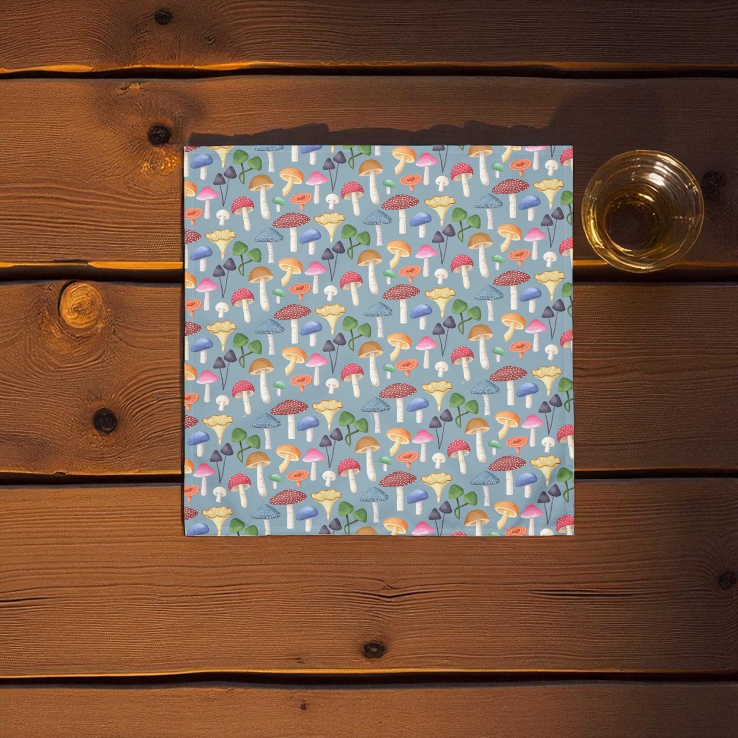 Blue mushroom themed napkin laying on a wooden table with a glass