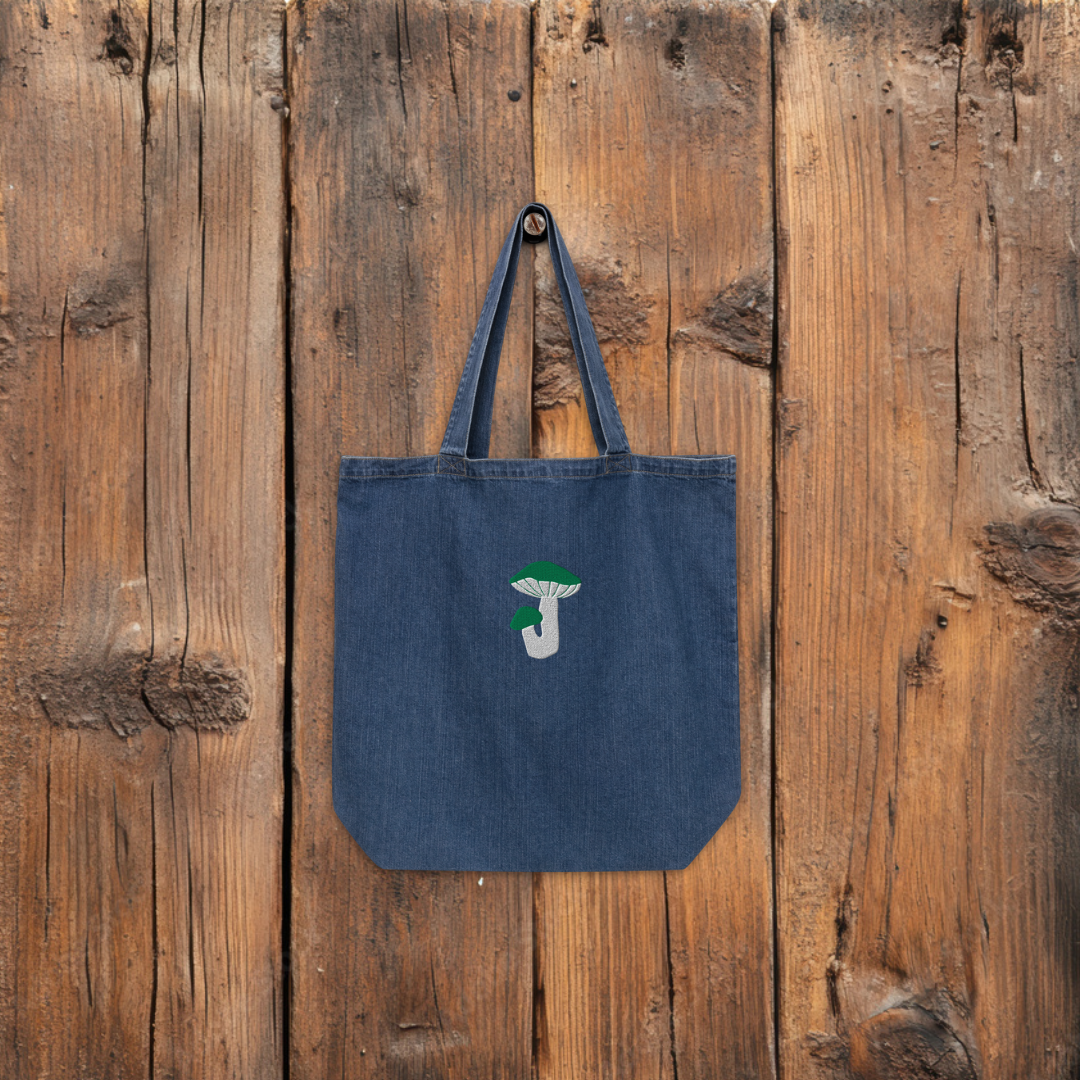 Denim tote bag green russula hanging from a wooden wall