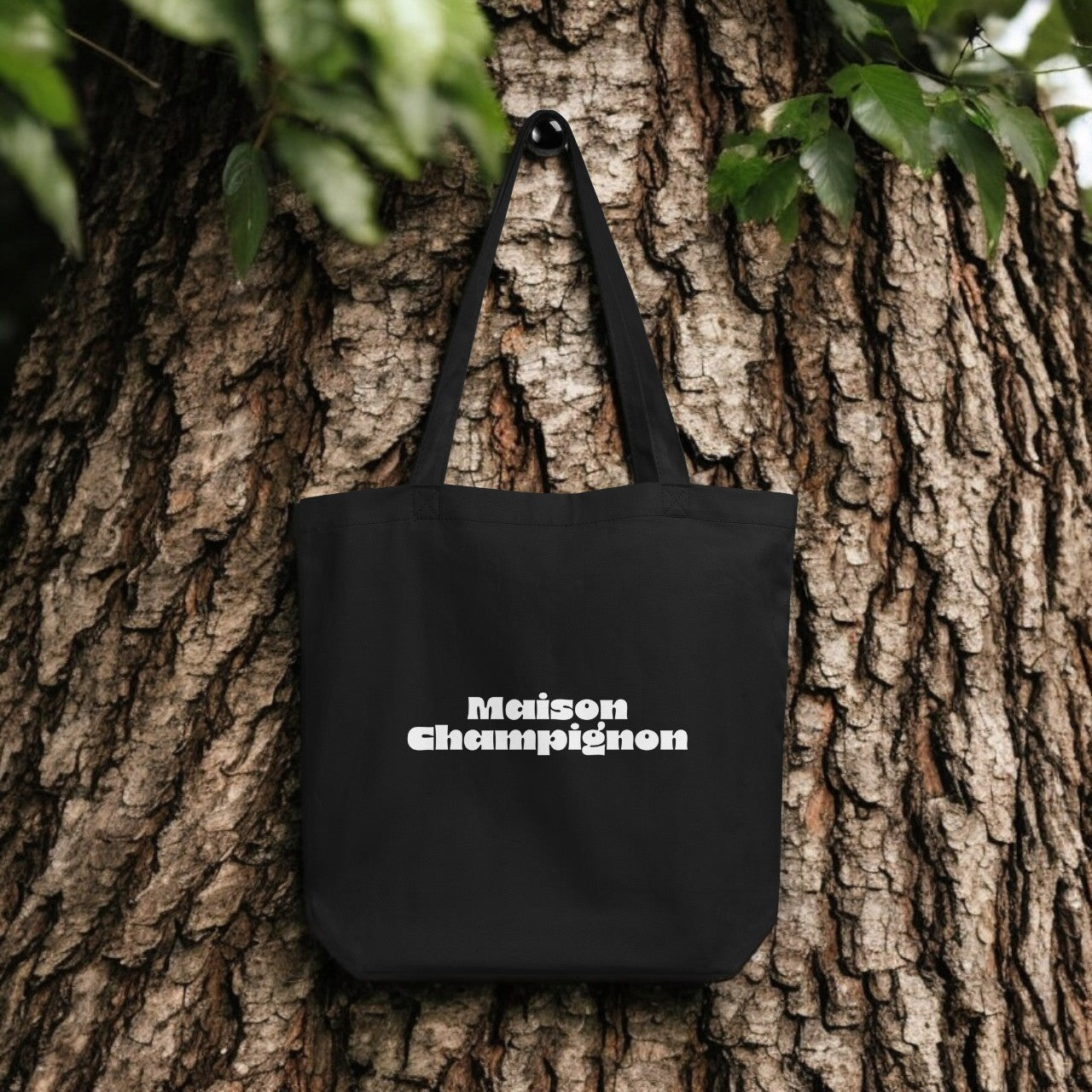 Maison Champignon Logo Tote Bag - black canvas with white logo print, outdoor setting.