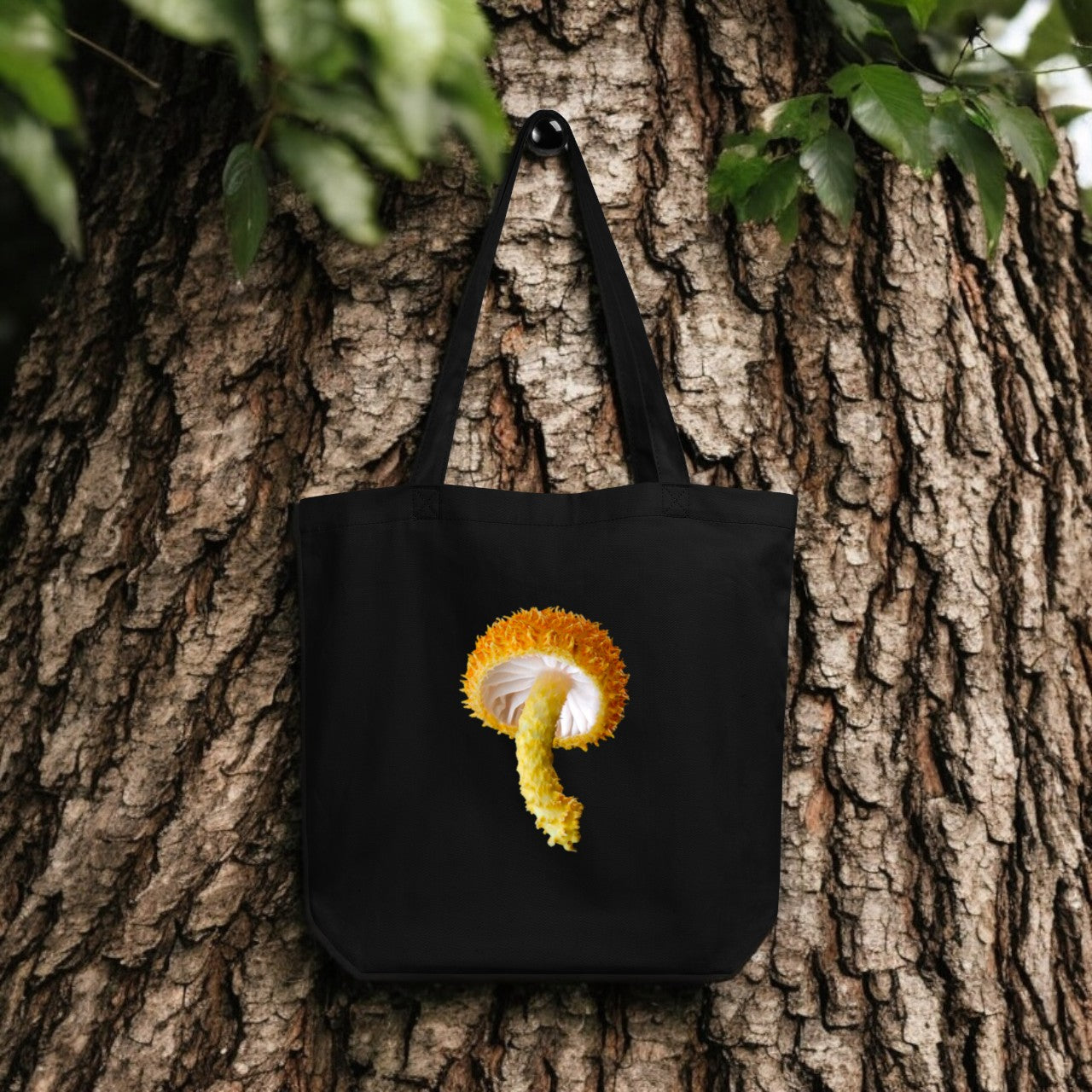 Cryptotrama Golden-Scruffy Collybia Tote Bag - black canvas with detailed mushroom underside print, outdoor setting.