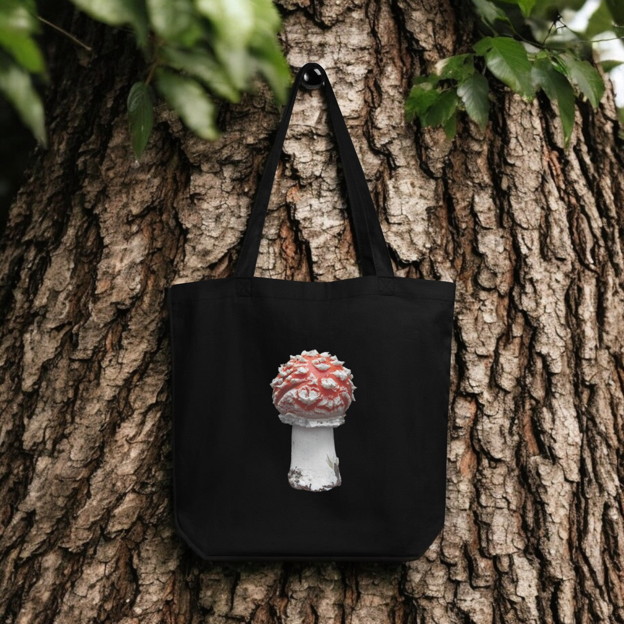 Amanita Muscaria Fly Agaric Tote Bag - black canvas with detailed mushroom underside print, outdoor setting.