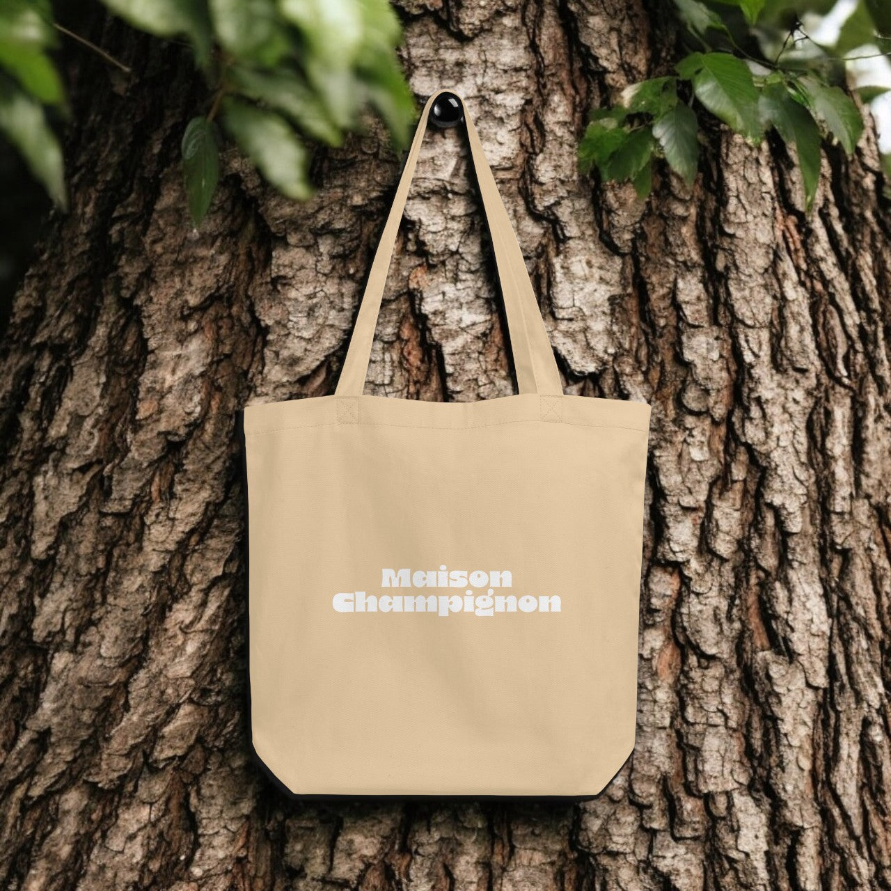 Maison Champignon Logo Tote Bag - beige canvas with white logo print, outdoor setting.