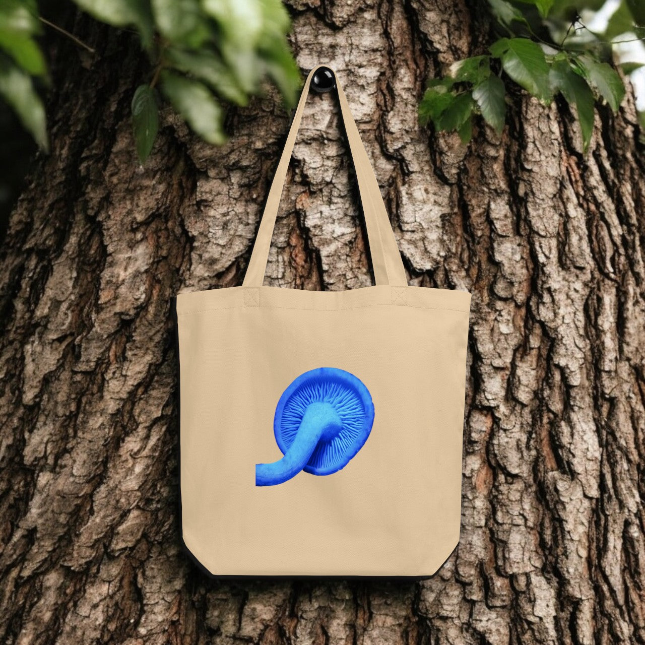 Rhodocollybia Blue Mushroom Tote Bag - beige canvas with detailed mushroom underside print, outdoor setting.
